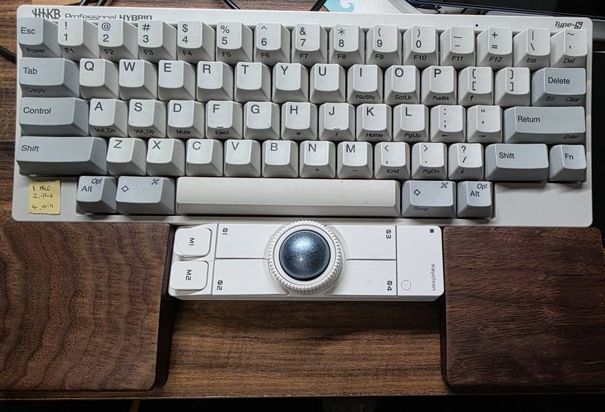 HHKBの手前にKeychron Nape Proを置き、左右に分かれた木製パームレストの真ん中に収めた机の上